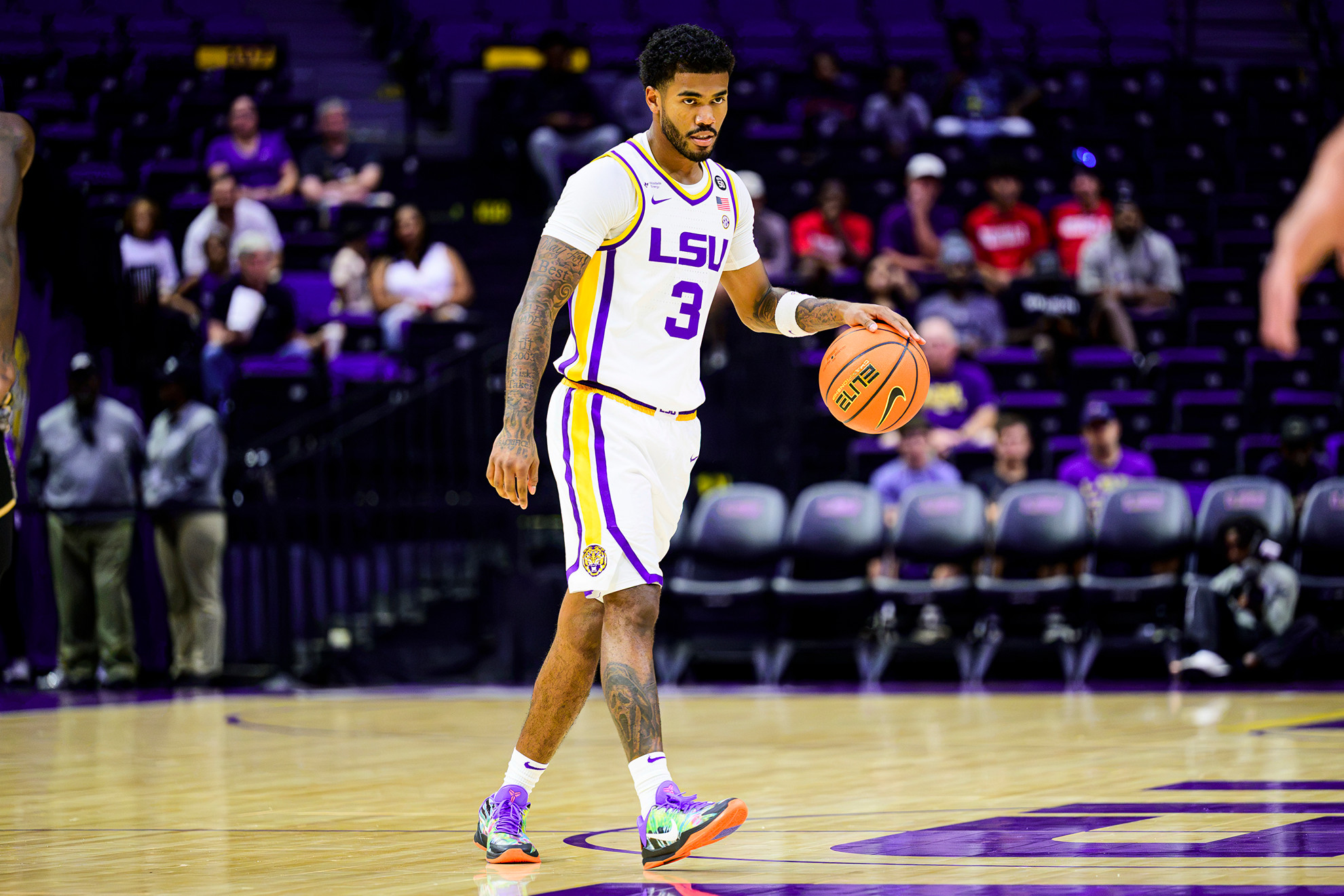 An athlete in an LSU jersey dribbles a basketball on a court during a game.